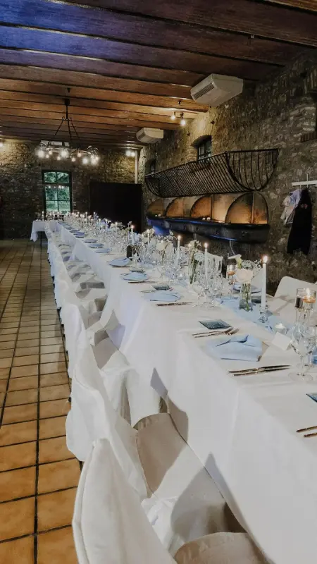 Salle de mariage voûtée en pierre : longues tables nappées de blanc – Les Anciennes Écuries, mariage de V et L, septembre 2025