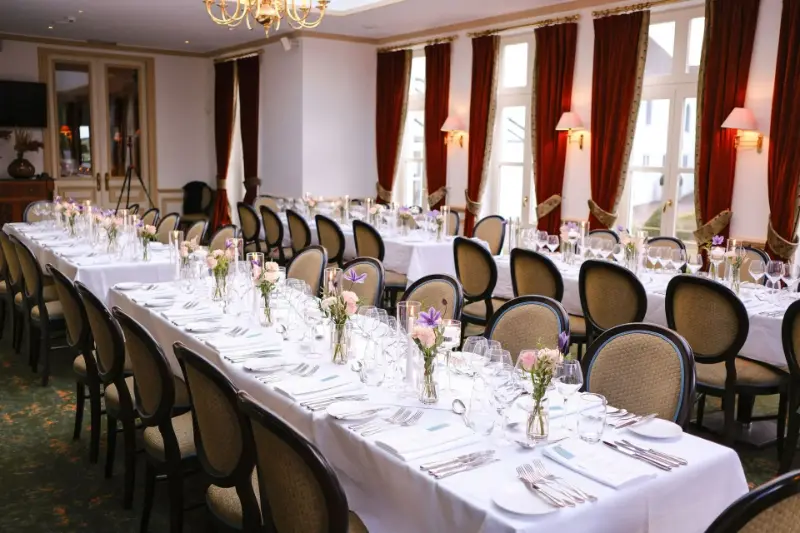Salle de réception de château : longues tables, chaises médaillon et petits bouquets – Golf Château de la Tournette, mariage de C et D, août 2025