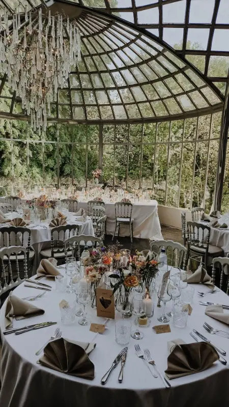 Réception sous verrière : tables rondes, chaises Napoléon noires et bouquets – Château de Ruisbroek, mariage de E et D, mai 2025