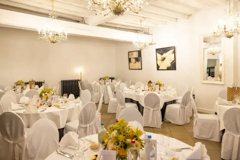 Salle blanche avec lustres : housses de chaise et bouquets jaunes – Salons de Romree, mariage de MC et K, octobre 2024