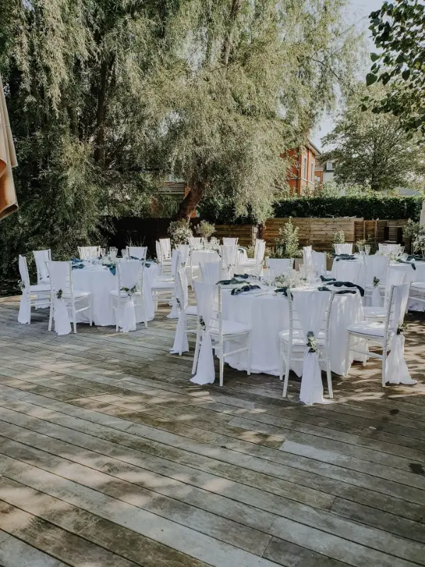 Réception de mariage en plein air : tables rondes et housses de chaise blanches sur terrasse – The Lodge, mariage de K et M, septembre 2024