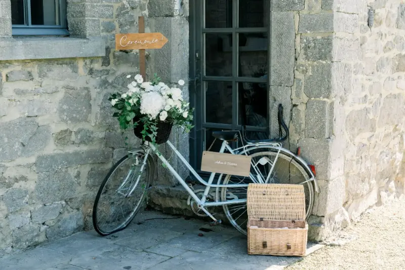 Décoration d'accueil champêtre : vélo vintage blanc fleuri, panier et panneau en bois – Ferme de la Haillebaude, mariage de V et A, septembre 2024