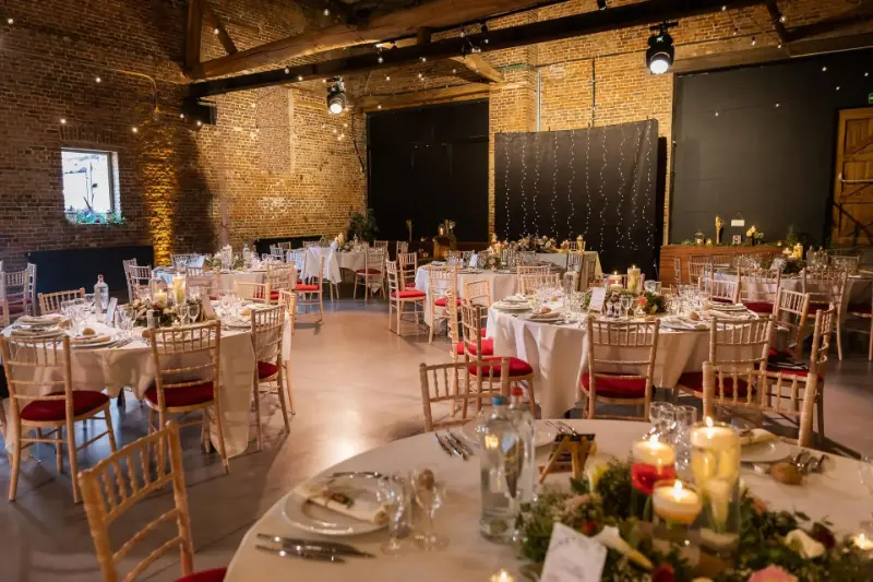 Salle en briques : tables rondes, chaises dorées et centres de table aux bougies – Hof Te Vitseroel, mariage de B et V, août 2024