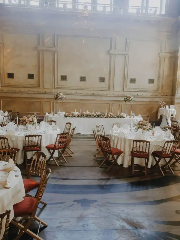 Salle à moulures décorée pour un mariage : tables rondes et chaises en bois – Palais de Plume, mariage, août 2024