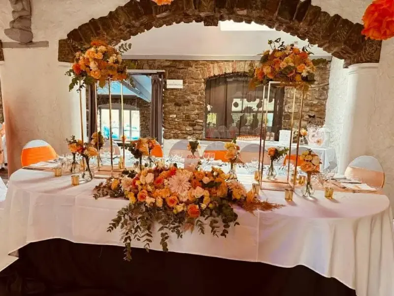 Table d'honneur sous une arche en briques avec compositions florales orange et pêche – Cense de Lalouette, mariage de M et L, août 2024