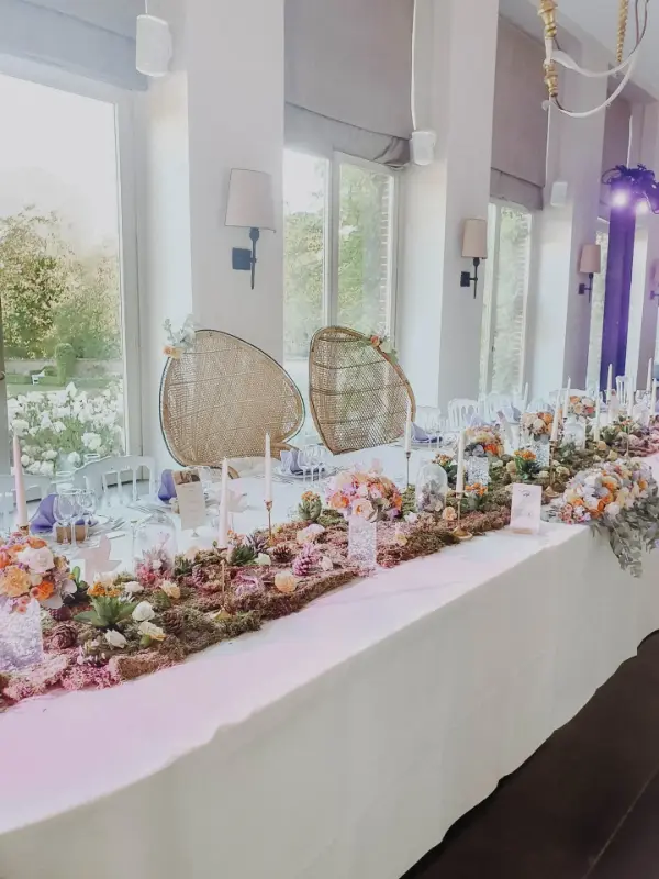 Table d'honneur avec chemin floral pastel et fauteuils en rotin – Domaine Franc Waret, mariage de L et L, août 2024
