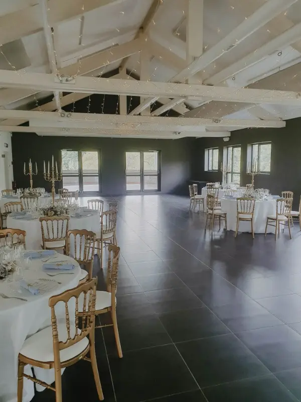 Salle à poutres blanches : tables rondes et chaises dorées – Domaine d'Arondeau, mariage de R et B, juillet 2024