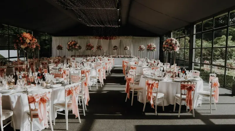 Salle de mariage avec voilage blanc, nœuds de chaise saumon et compositions roses – Château de Terblock, mariage de L et M, juin 2024