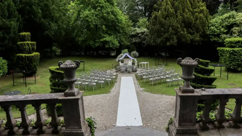 Cérémonie laïque dans un jardin : allée blanche, chaises et vases sur socles – Château de Ruisbroek, mariage de E et J, juin 2024