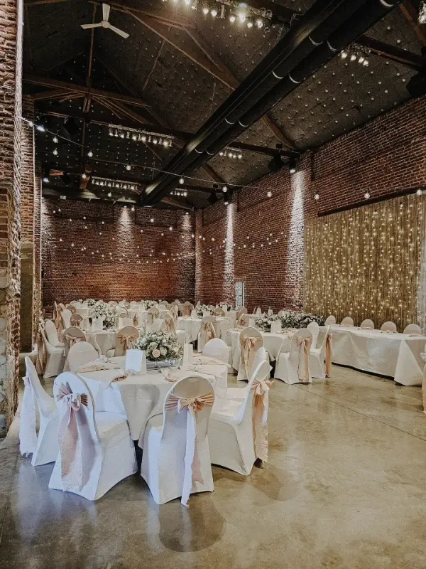 Grange en briques avec rideau lumineux et housses de chaise à nœuds pêche – Ferme de Bertinchamps, mariage de C et J, juin 2024