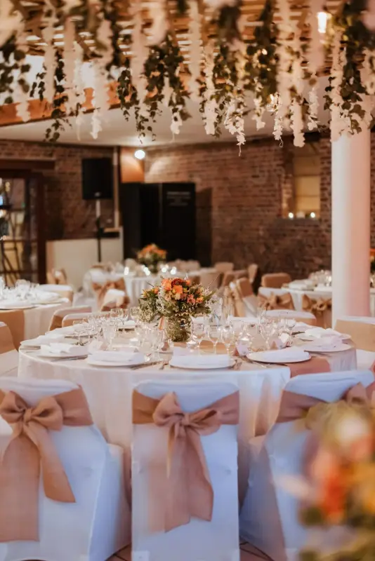 Salle en briques : centres de table en fleurs orange et pêche – Ferme des Oliviers, mariage de C et Y, octobre 2023
