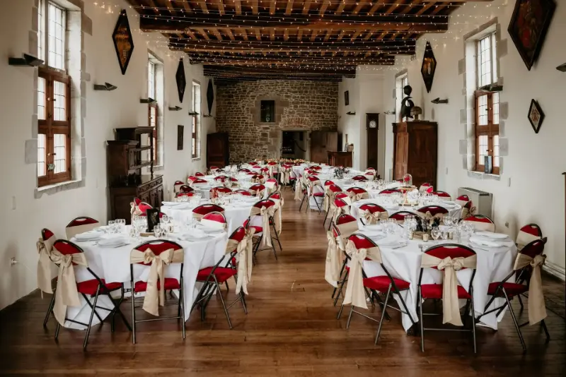 Salle à poutres : housses de chaise blanches et nœuds rouges – Château-Fort de Feluy, mariage de L et A, octobre 2023