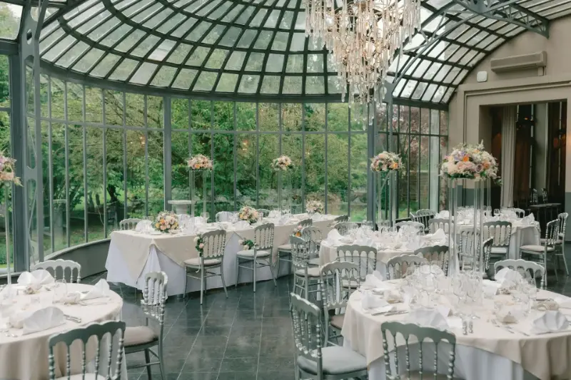 Orangerie avec lustre en cristal : tables rondes et compositions florales – Château de Ruisbroek, mariage de C et S, septembre 2023