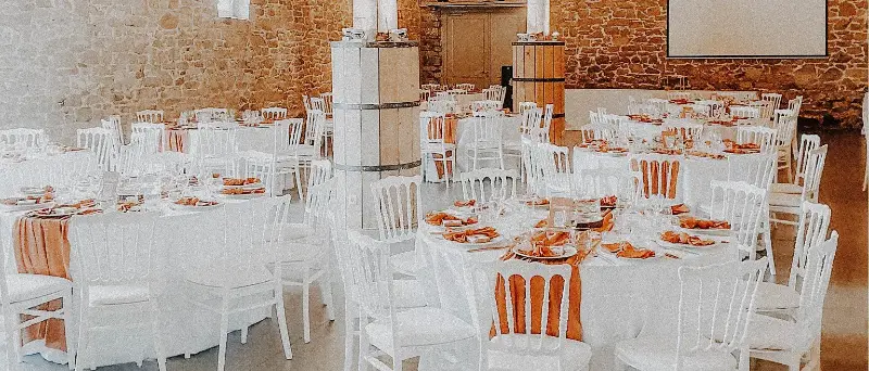 Salle en briques : chaises Napoléon blanches et serviettes orange – Domaine d'Achêne, mariage de m et T, août 2023