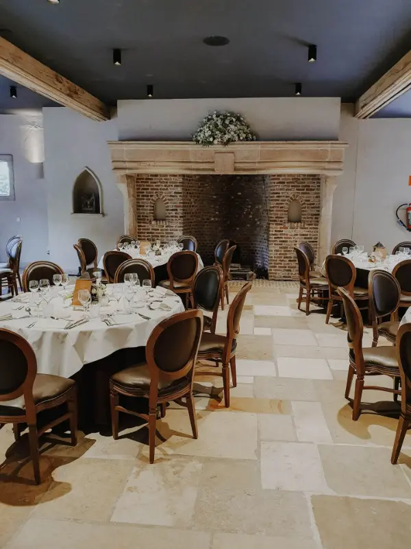 Salle avec cheminée en pierre : tables rondes et chaises médaillon en bois – Waerboom, mariage de S et B, août 2023