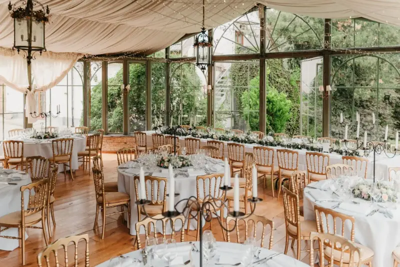 Véranda décorée de voilages : lanternes, candélabres et tables rondes – Abbaye de Nizelles, mariage de B et T, juillet 2023