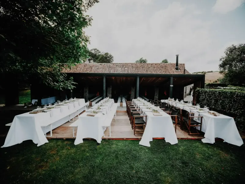 Réception en extérieur sous préau : longues tables nappées de blanc – La Carrière, mariage de M et Y, juillet 2023