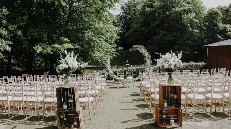 Cérémonie laïque dans un jardin : chaises Napoléon, caisses en bois et arche fleurie – Chalet de Robinson, mariage de M et F, mai 2023