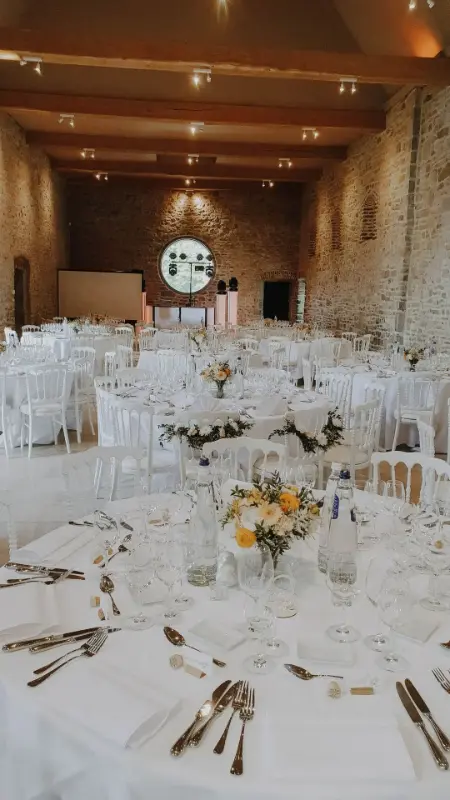 Salle en briques : tables rondes et centres de table jaunes – Château de Lavaux-Sainte-Anne, mariage de O et S, mai 2023