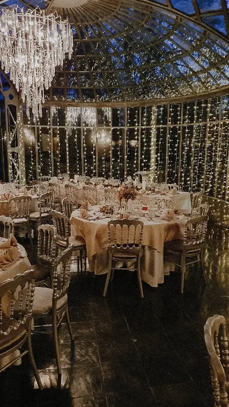 Salle avec rideaux lumineux : tables rondes et chaises Napoléon – Château de Ruisbroek, mariage de M et S, novembre 2022
