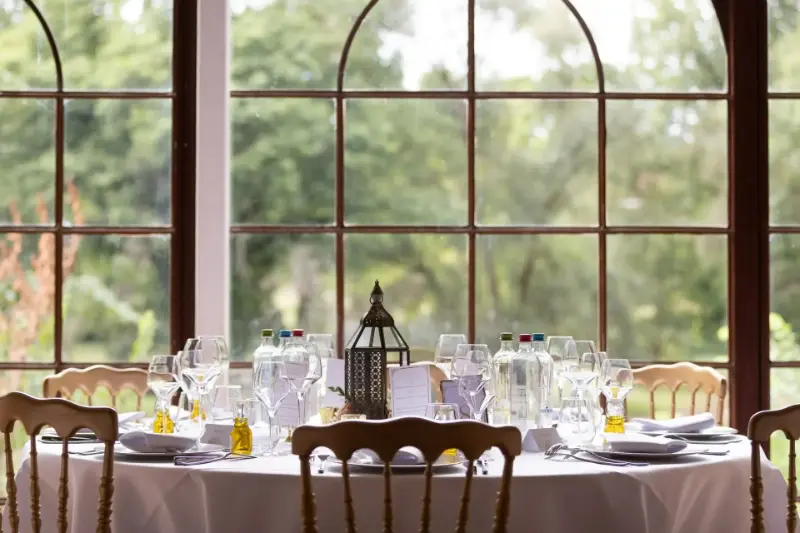 Table ronde dressée devant une fenêtre en arc avec lanterne – Château de Grand-Bigard, mariage de S et J, juillet 2022
