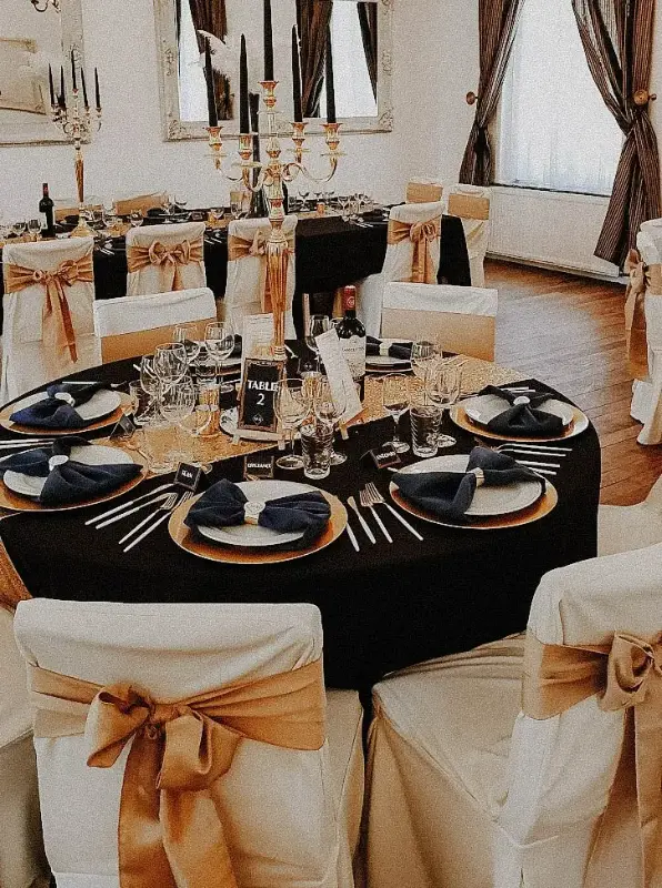 Table élégante : nappe noire, sous-assiettes dorées et serviettes bleu marine – Château de la Rozerie, mariage de M et K, juin 2022