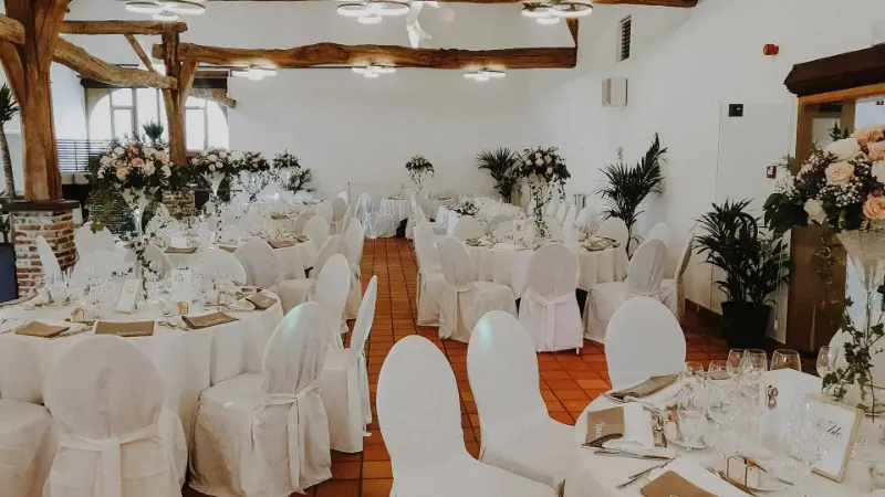 Salle avec housses de chaise blanches, tables rondes et plantes – Hof Ter Musschen, mariage de L et M, avril 2022