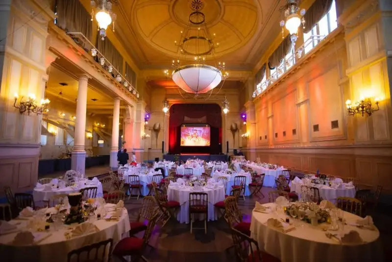 Salle de bal historique avec scène : tables rondes décorées – Palais de Plume, mariage de m et T, septembre 2021